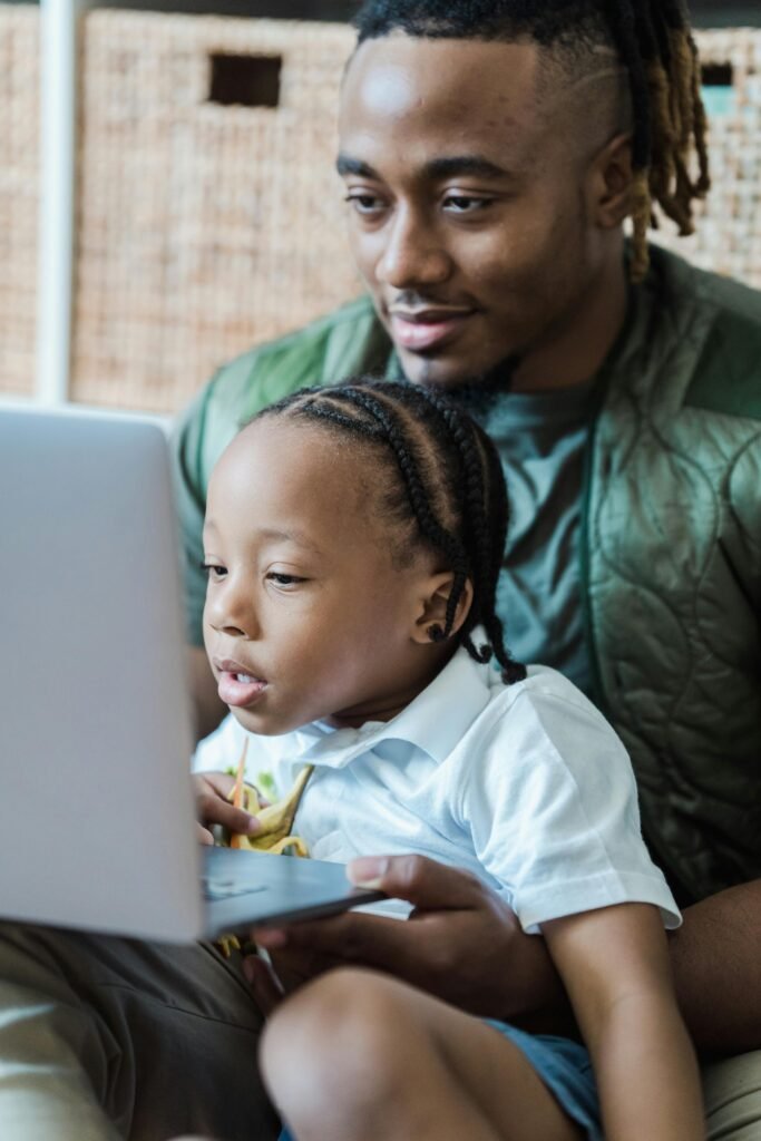 A father and child bonding while using a laptop indoors, showcasing family and technology.