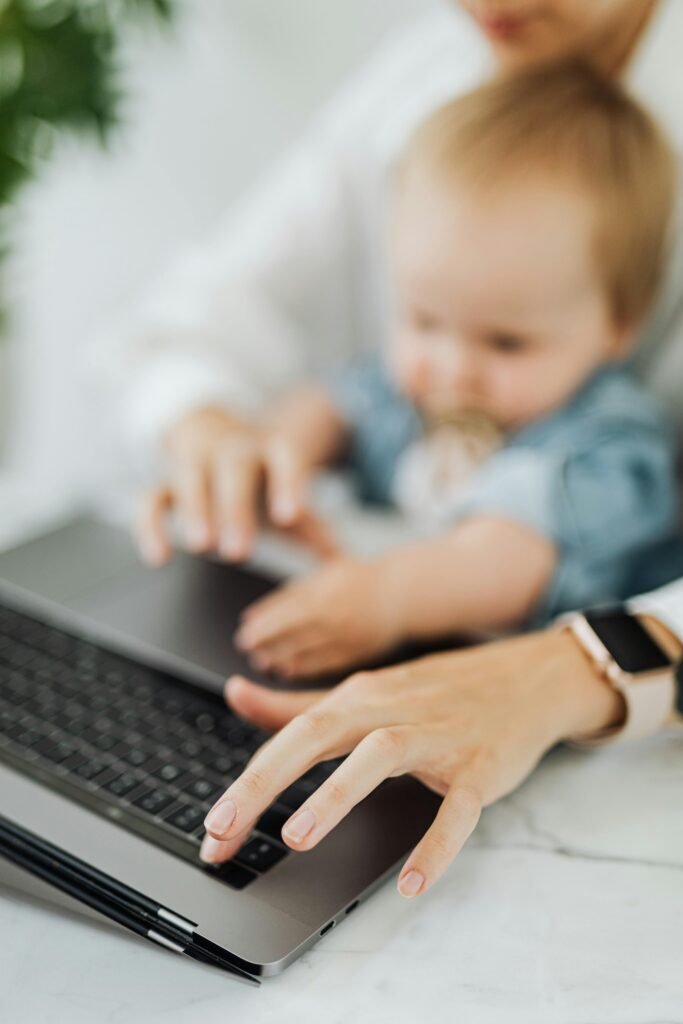 A mother and her baby engage with a laptop, showcasing multitasking in a modern workspace.
